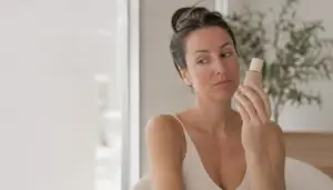 Woman with post-microneedling flushed skin holding makeup foundation, considering when it's safe to wear makeup after treatment